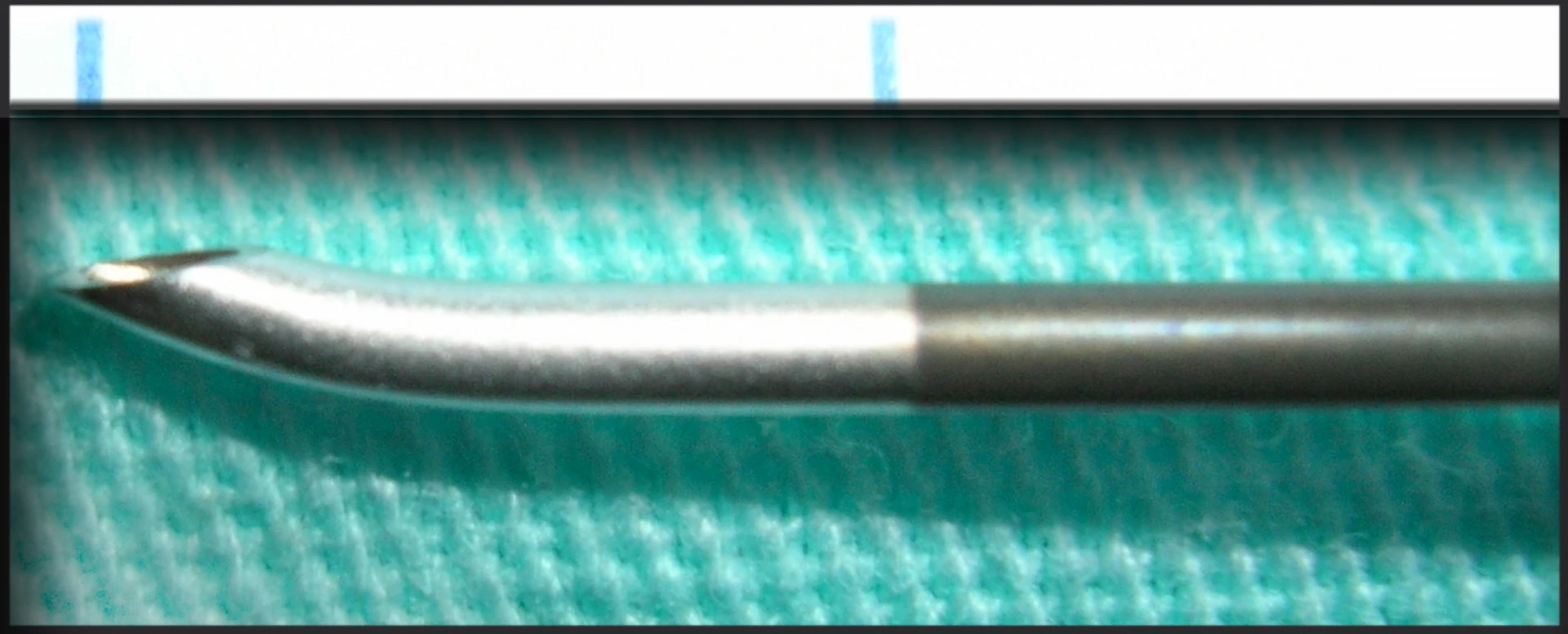 Macro close-up of a Tuohy needle tip showing the curved Huber bevel that directs the catheter cephalad through the dura